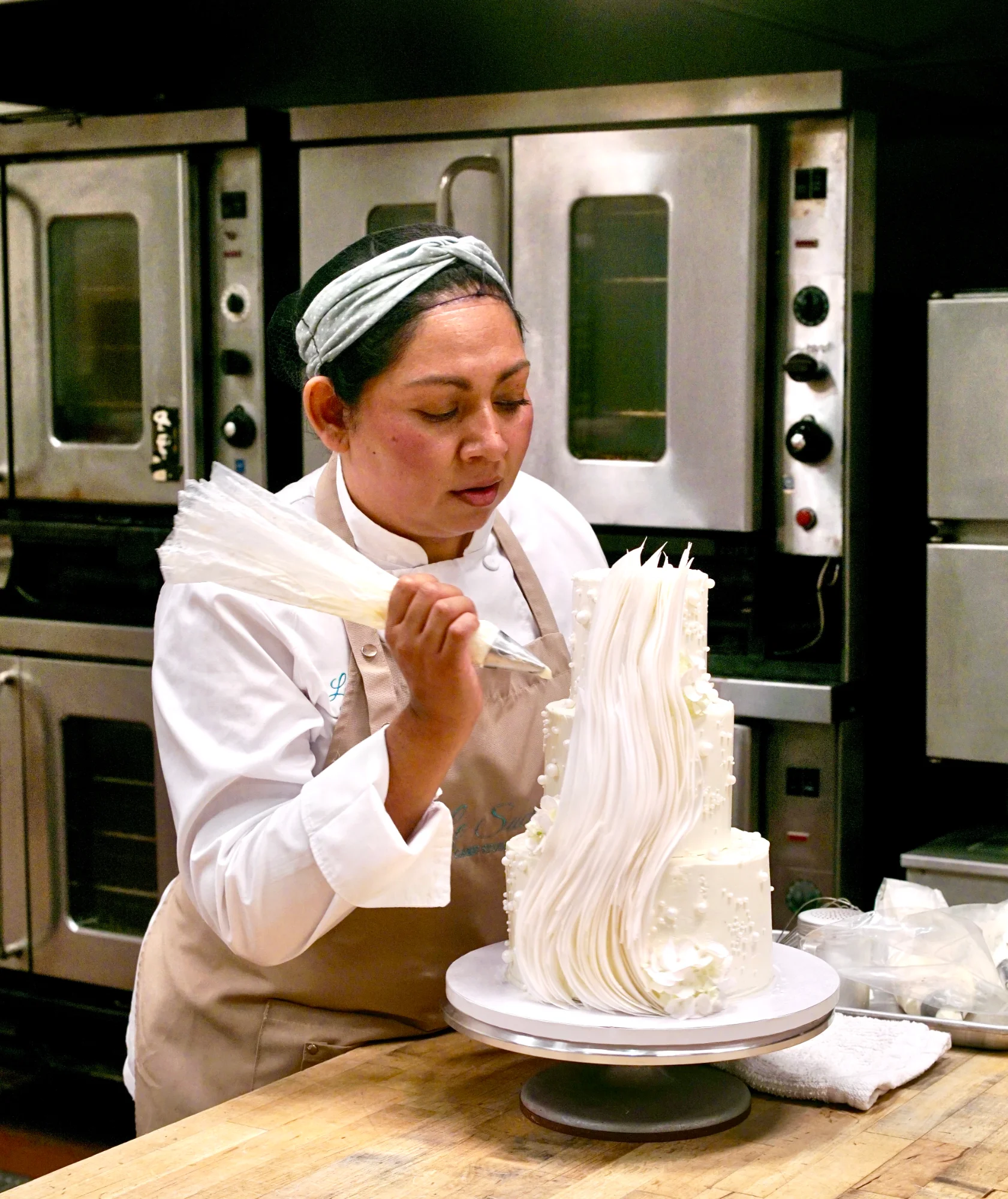 Pastry chef piping buttercream onto a cake in a sunlit kitchen